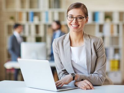 Immagine che mostra una ragazza sorridente sui 35 anni mentre è al computer. È usata come immagine del corso gratuito "SEGRETARIO/A" del progetto GOL